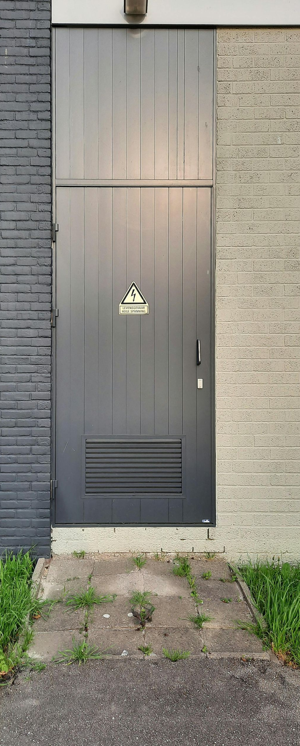 A gray metal door on a building with a textured stone facade and a small concrete walkway.