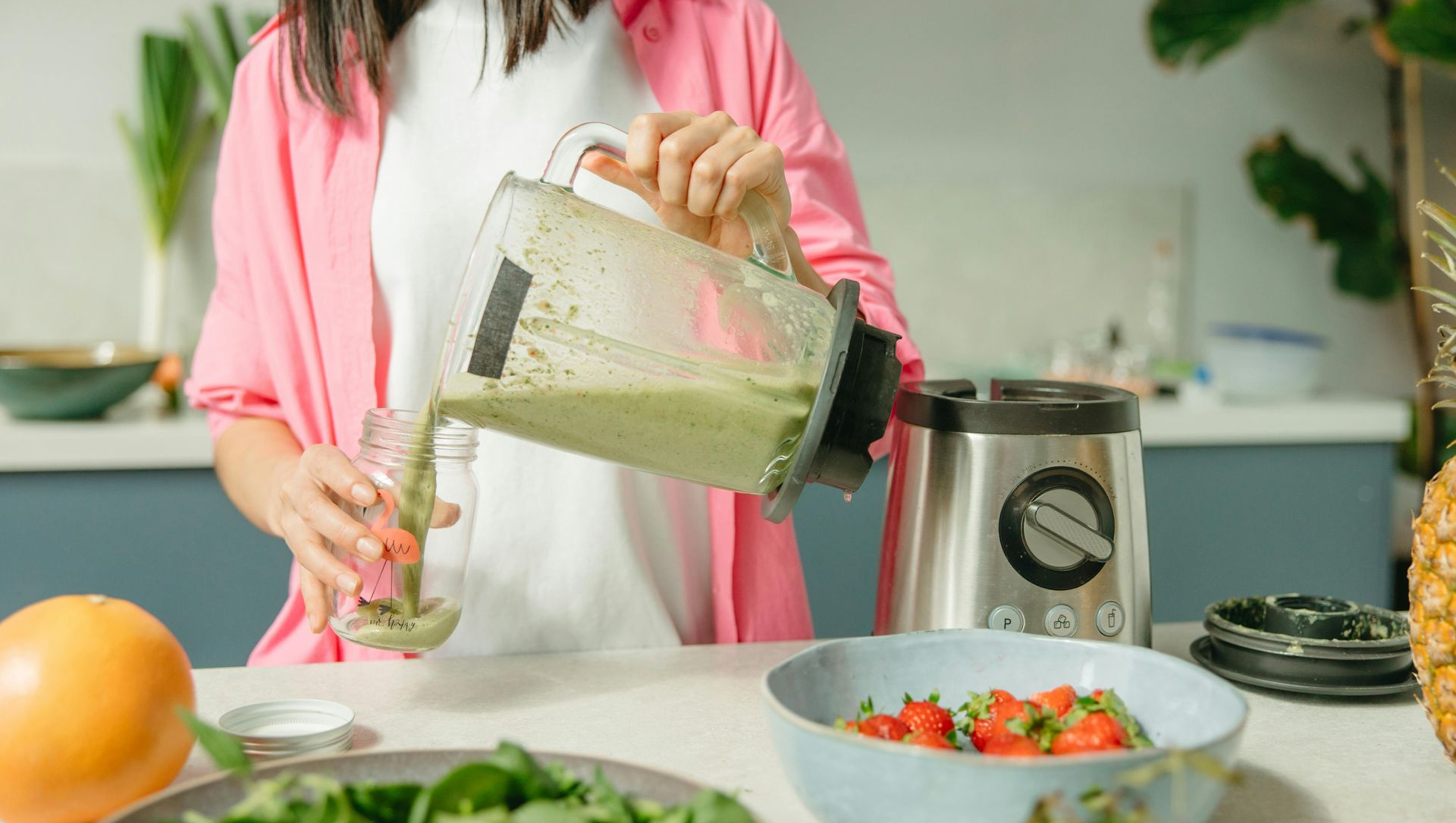 Woman pours green smoothie from blender into glass in kitchen.