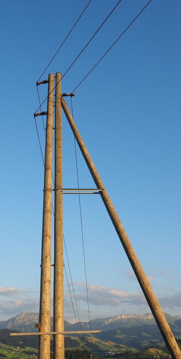Wooden utility pole with wires against a blue sky, mountain range in background.