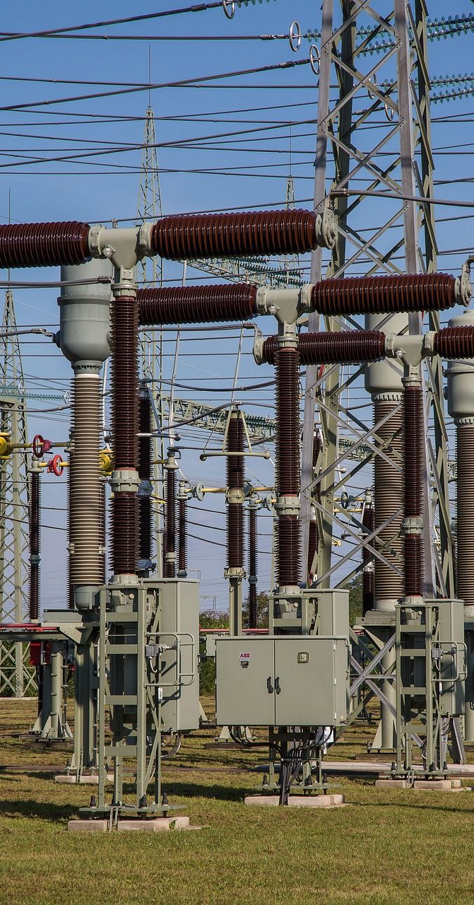 Electrical power substation with tall insulators and metal structures against a blue sky.
