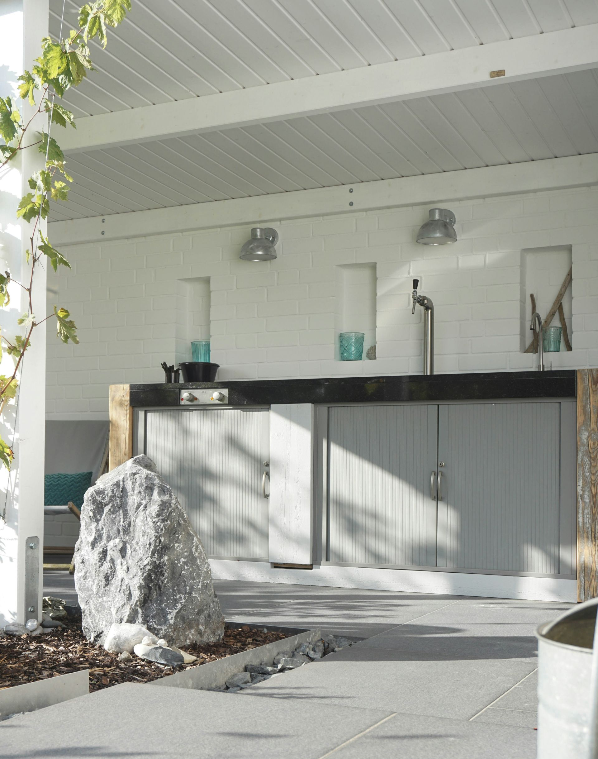 Outdoor bar with white walls, gray cabinets, tap, and decorative rock.