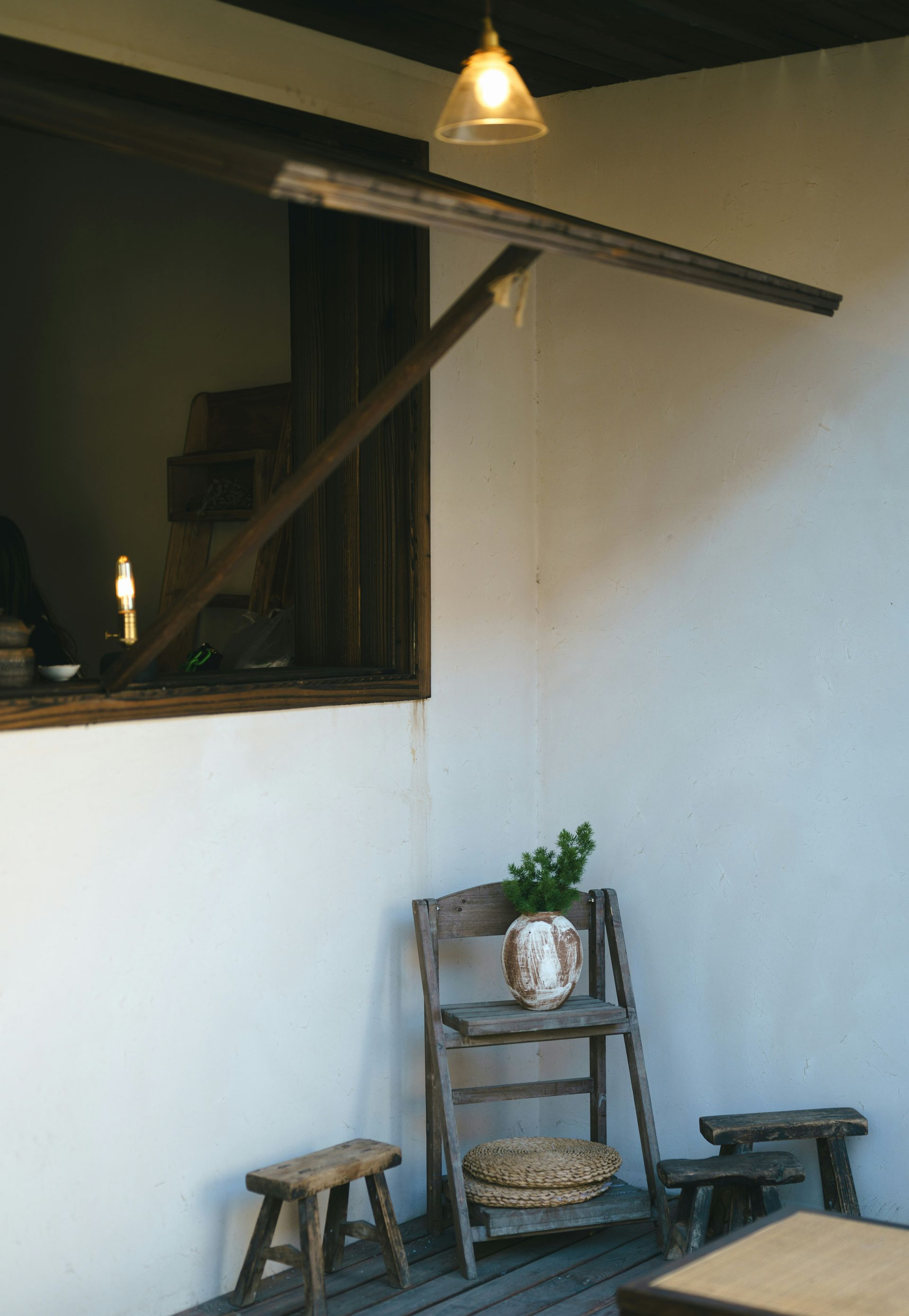 Corner room with wooden furniture: small stools, a tiered shelf, and a table, all on a wooden deck.