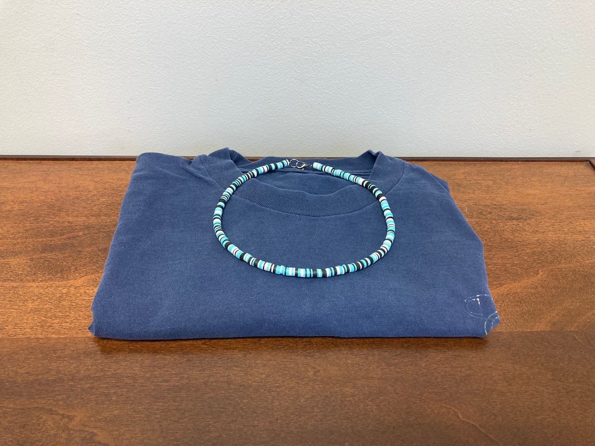 Blue shirt on a brown surface with a necklace of blue, black, and white beads draped across it.