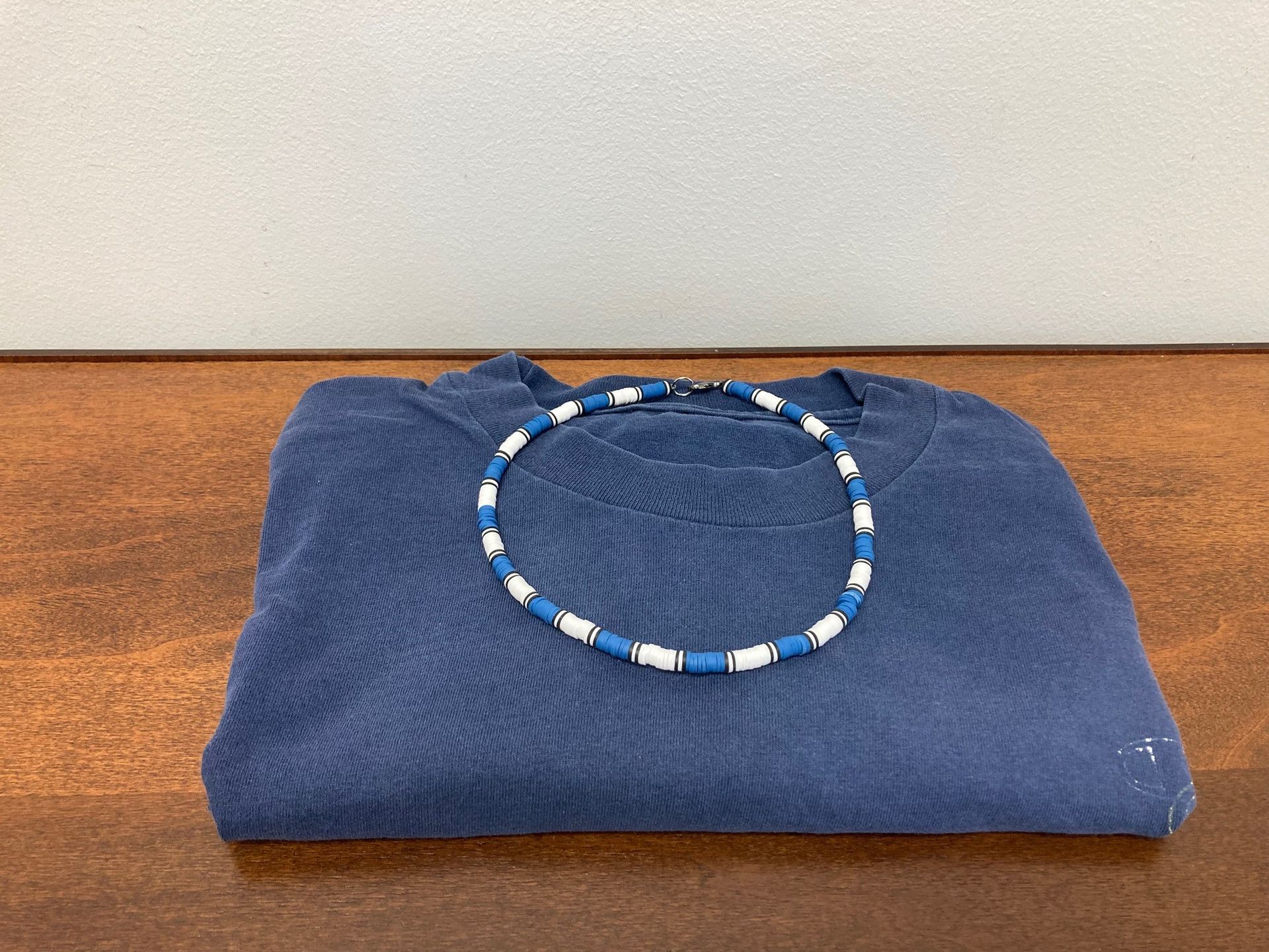 Blue folded shirt with a blue and white beaded necklace.