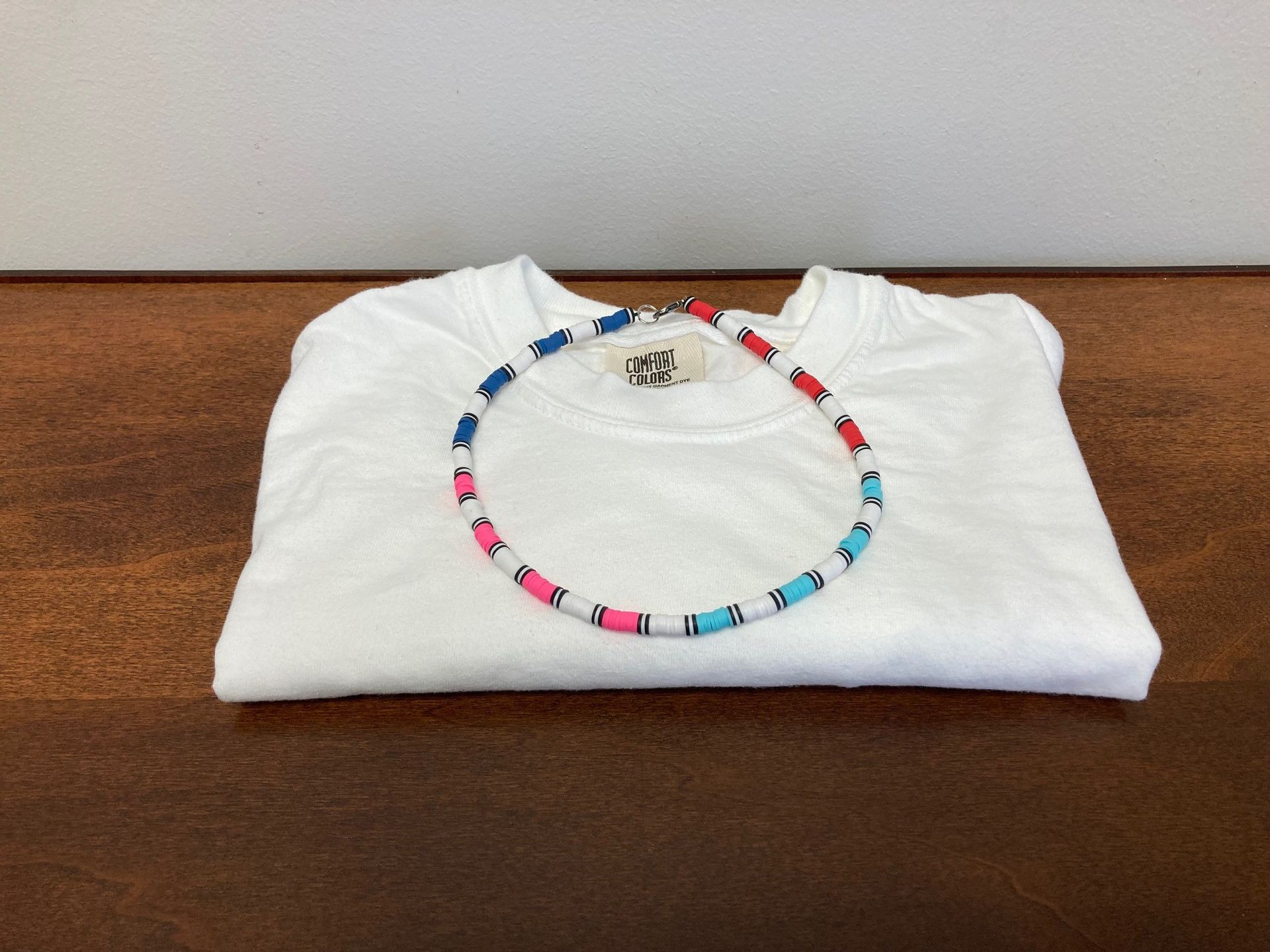 White folded shirt with a colorful beaded necklace on a brown surface.
