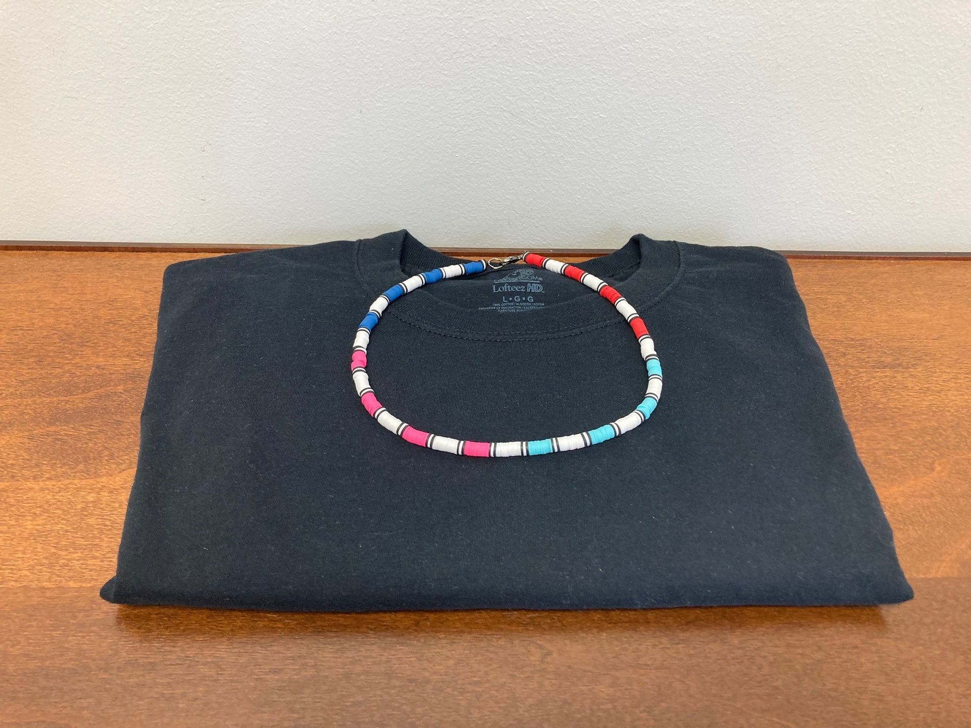 Black folded t-shirt on a wooden surface with a colorful beaded necklace on top.