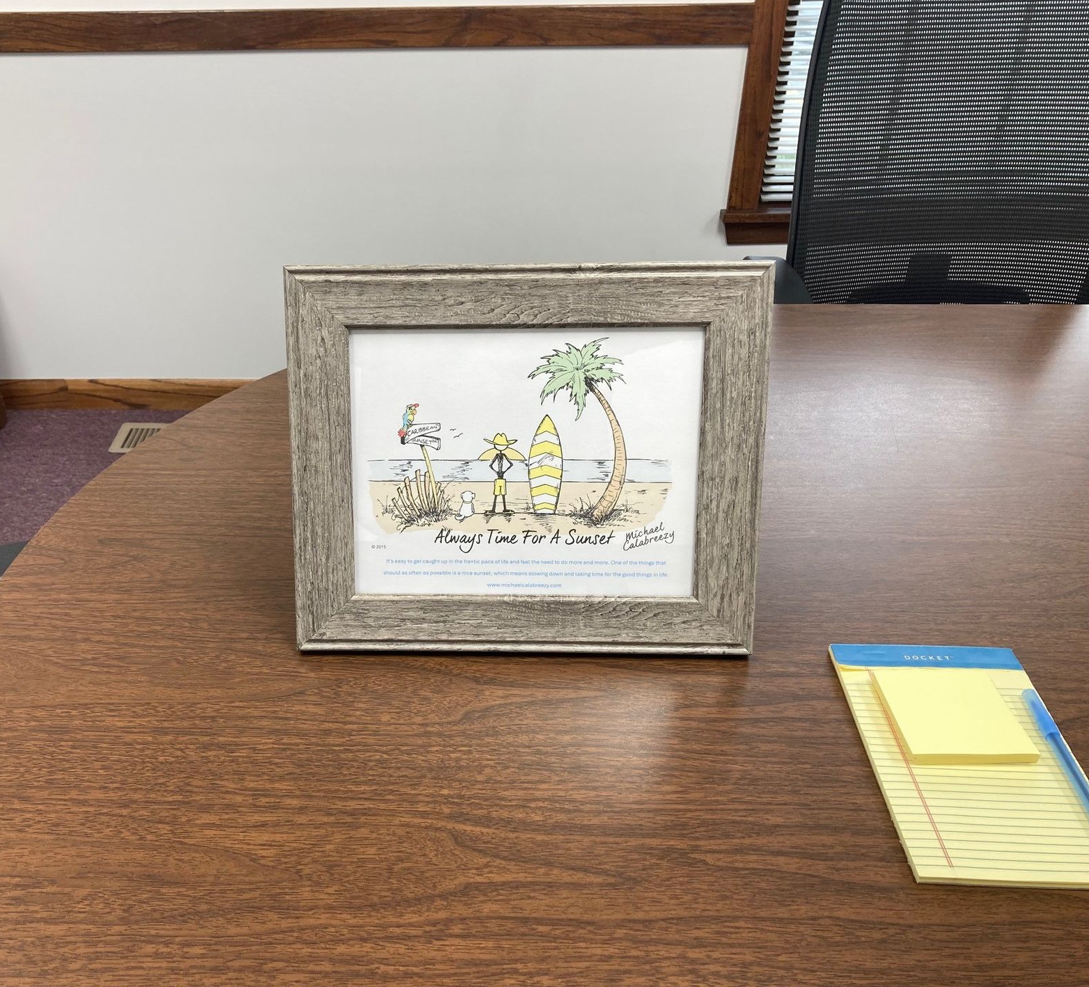 Framed artwork on a desk depicts a cartoon image of a beach scene.
