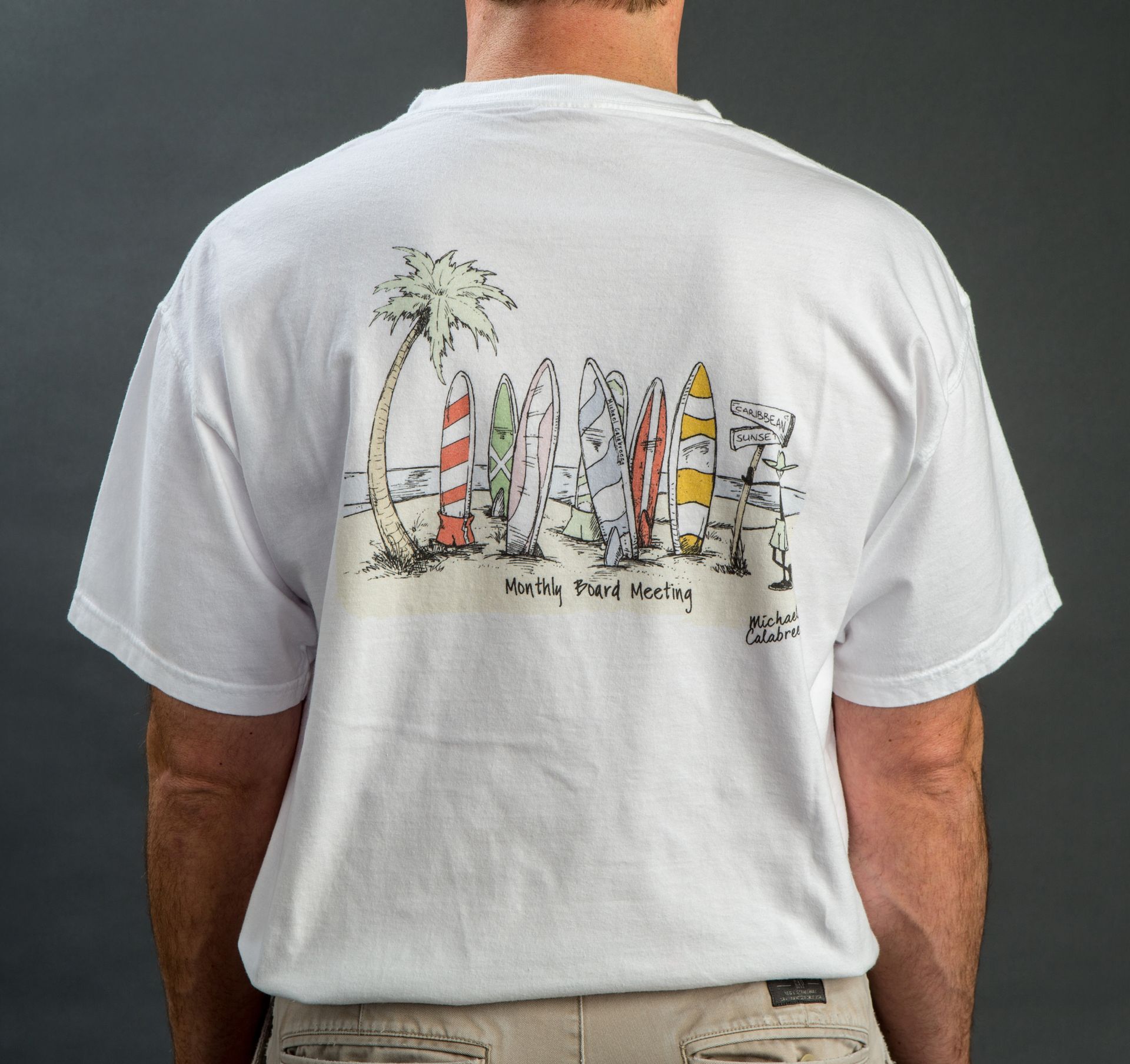 Back of a white t-shirt with a beach scene: palm tree, surfboards, and text 