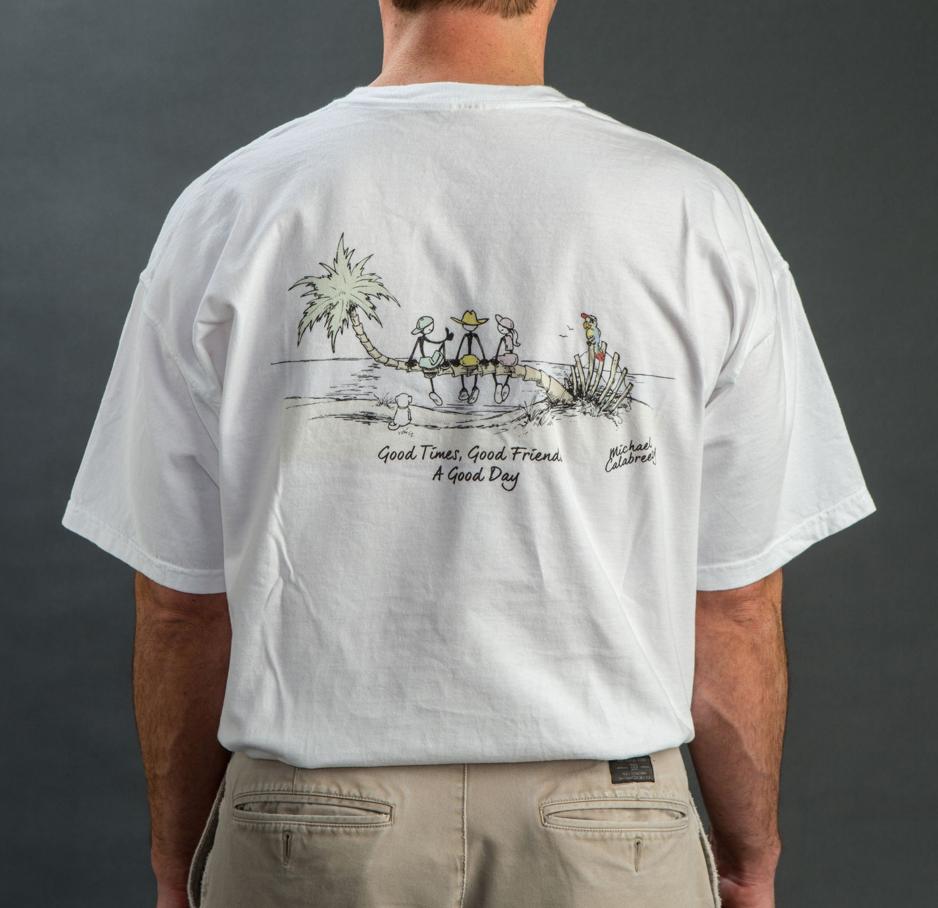 Back view of a person wearing a white t-shirt with a beach scene and text that says