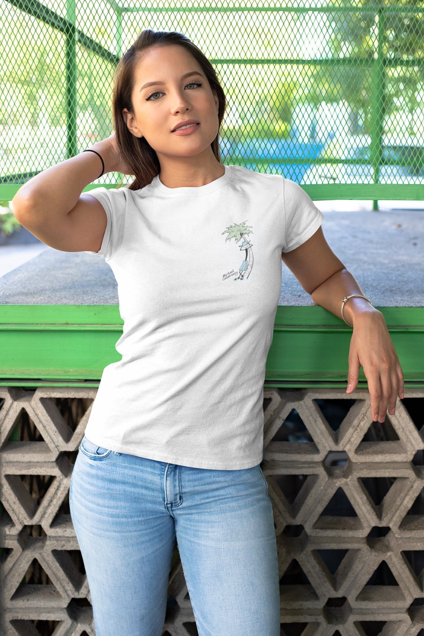 Woman in white t-shirt and jeans leaning against a green and gray wall, smiling.