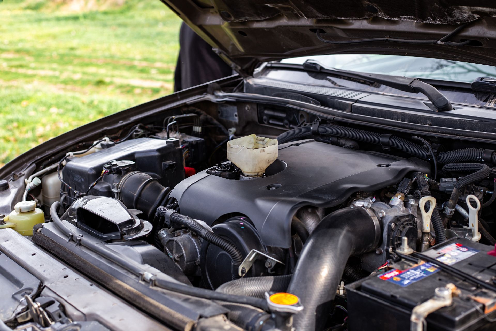 An open hood of a car revealing the engine bay, with a funnel placed in the oil filler port.