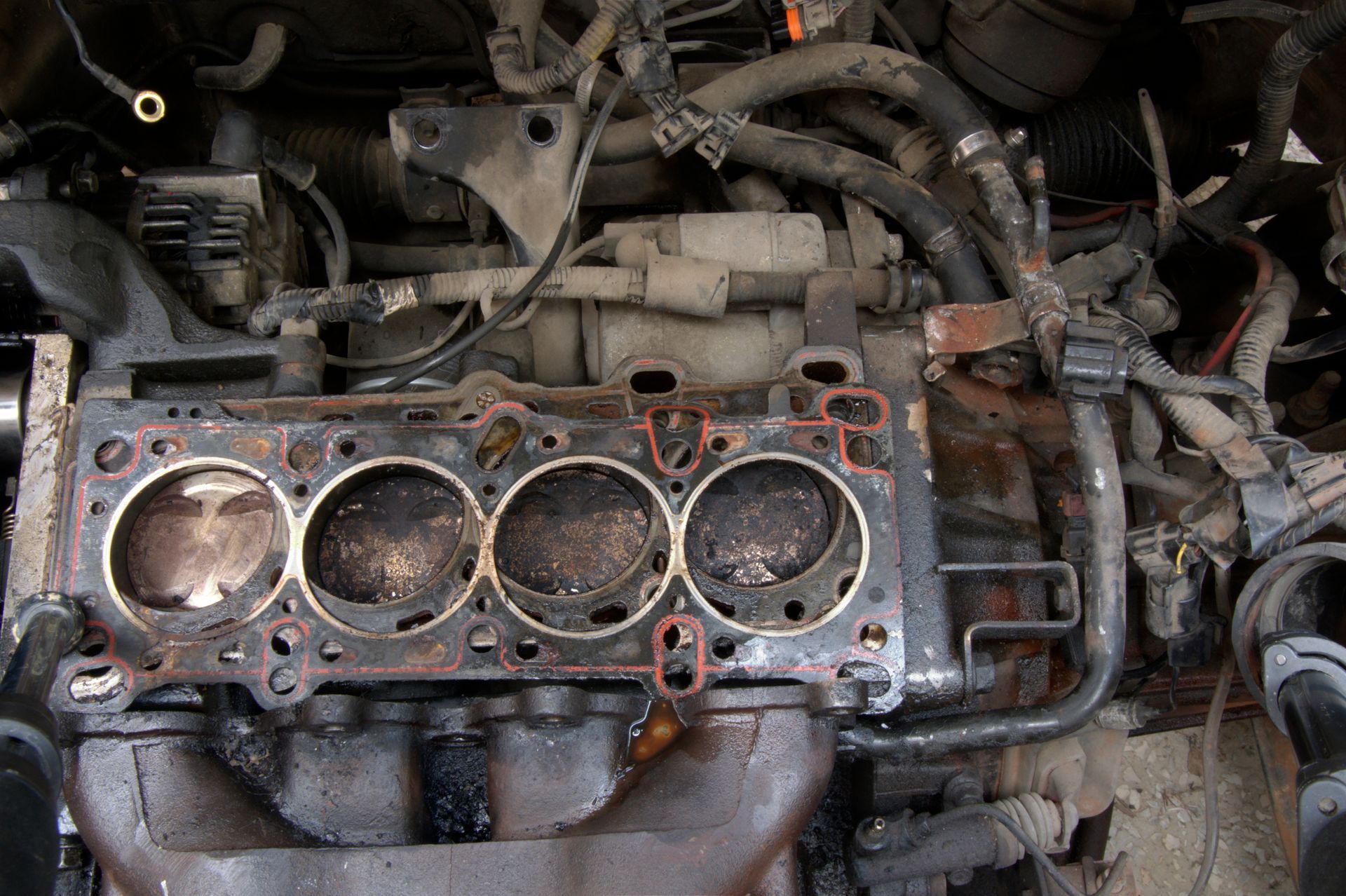 An exposed engine block with four cylinders and a head gasket, viewed from above within a car's engine bay.