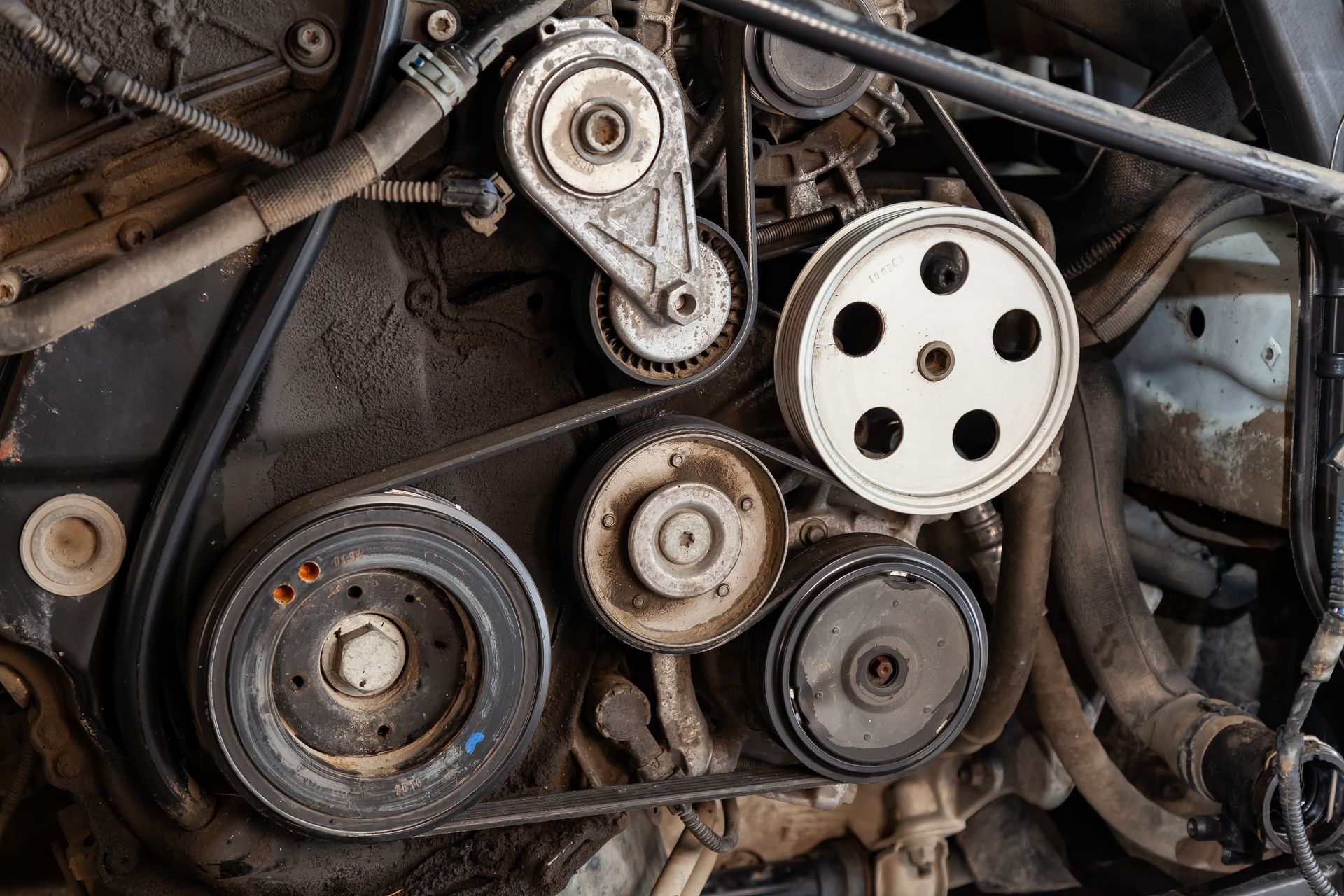 A close-up view of a car engine's serpentine belt system, featuring multiple circular pulleys and tensioners.
