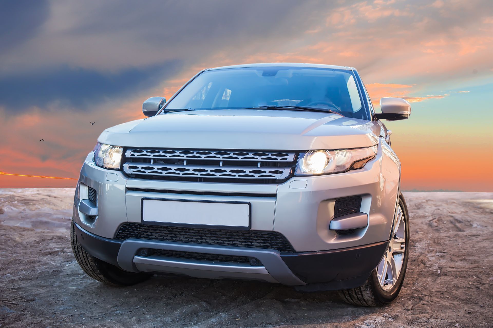 A white vehicle with its hood open and front bumper removed is undergoing repairs in an auto service garage.