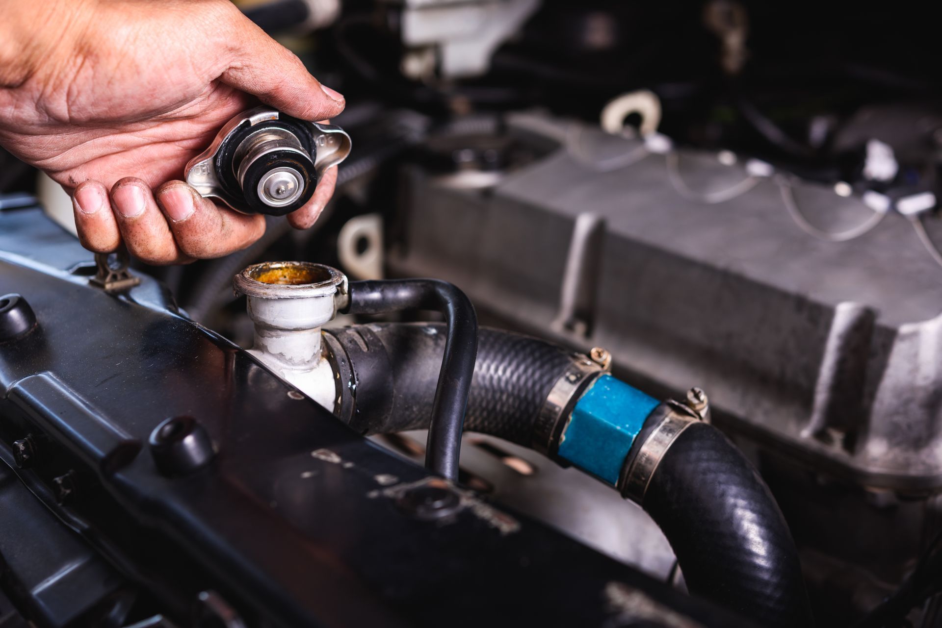 A hand holds a car radiator cap open above the cooling system filler neck in a vehicle engine bay.