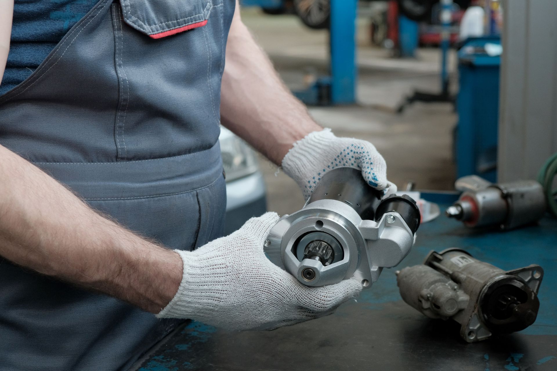 A mechanic wearing gloves examines a new car starter motor in an auto repair shop.