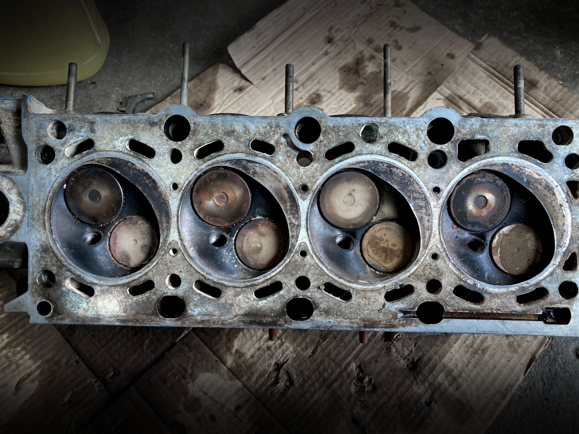 An overhead view of a dirty, removed four-cylinder engine cylinder head resting on cardboard.