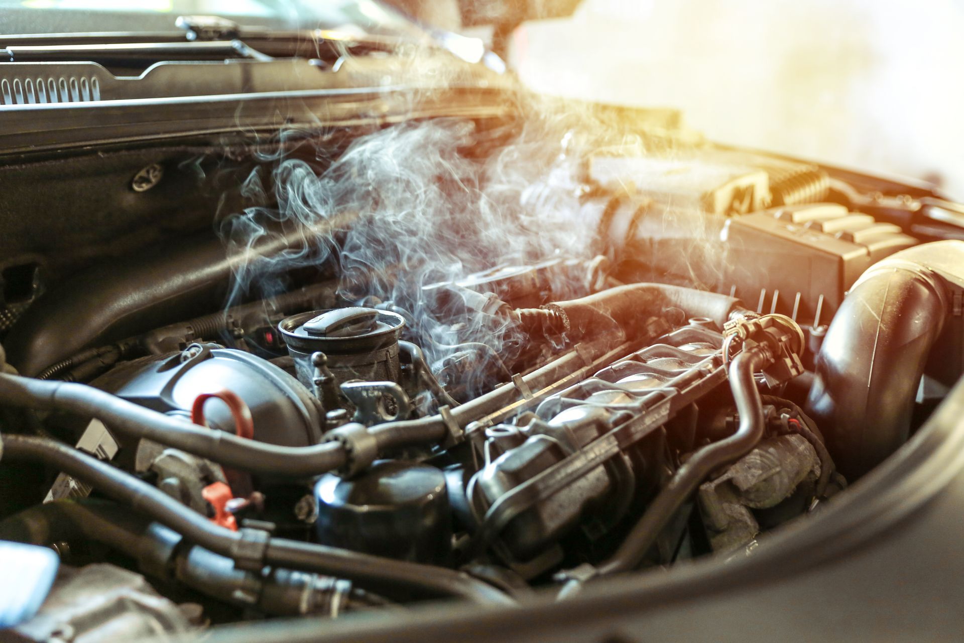 Smoke billows from the open hood of a car engine, indicating a vehicle breakdown or overheating.