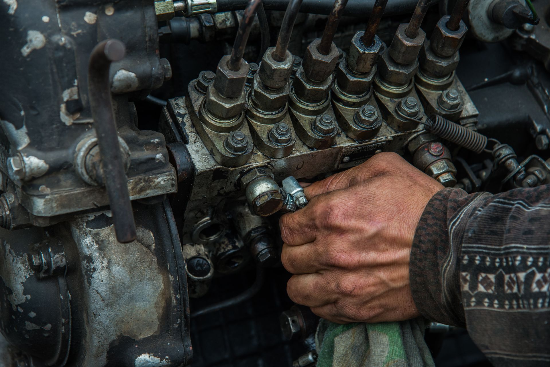 A mechanic’s hand works on the fuel injection pump of a dirty, metallic engine block.