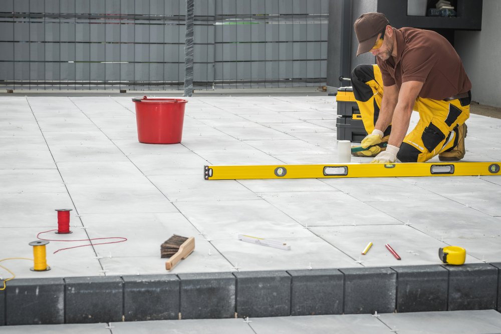A man is using a yellow level to level a tile floor.