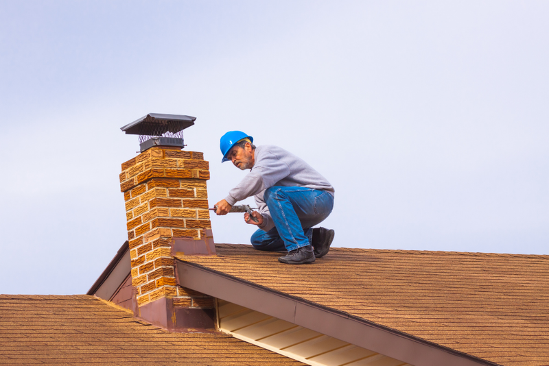 A man is kneeling on top of a roof fixing a chimney.