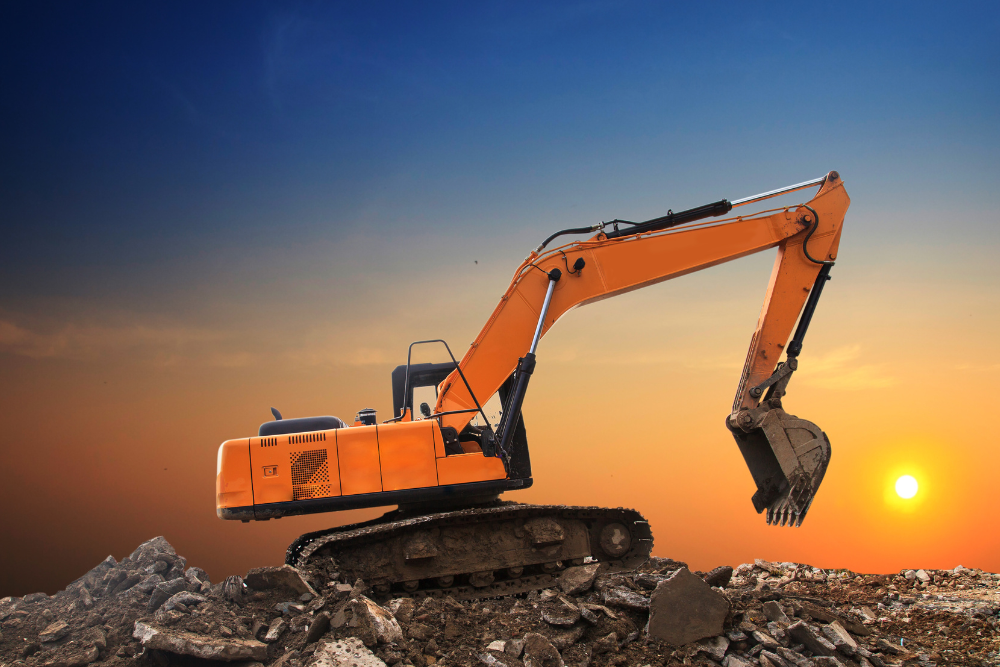 An orange excavator is sitting on top of a pile of rocks at sunset.