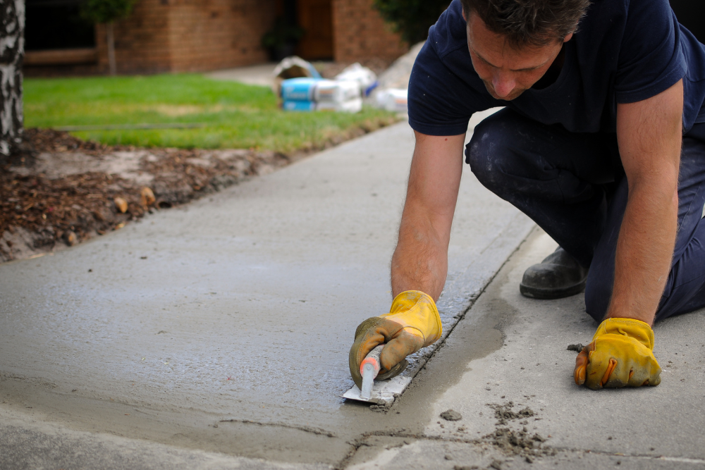 A man is kneeling down and spreading concrete on a sidewalk.