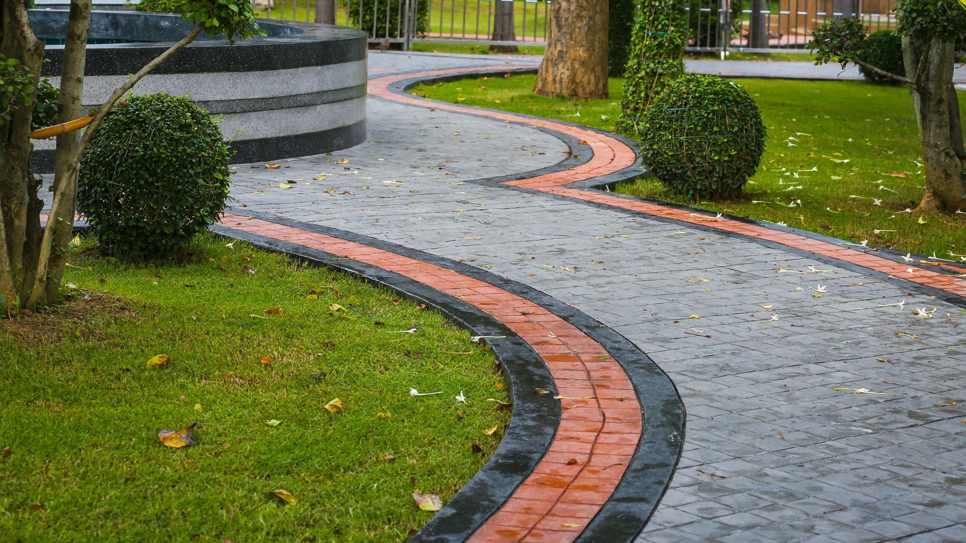 A brick walkway in a park surrounded by grass and trees.