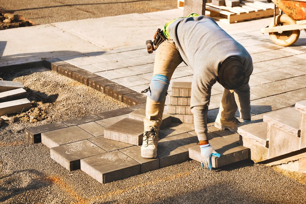 A man is laying bricks on a sidewalk.