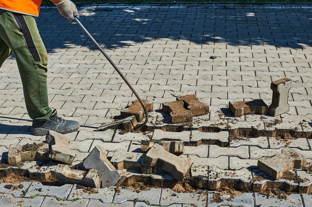 A man is digging a hole in a brick pavement with a shovel.