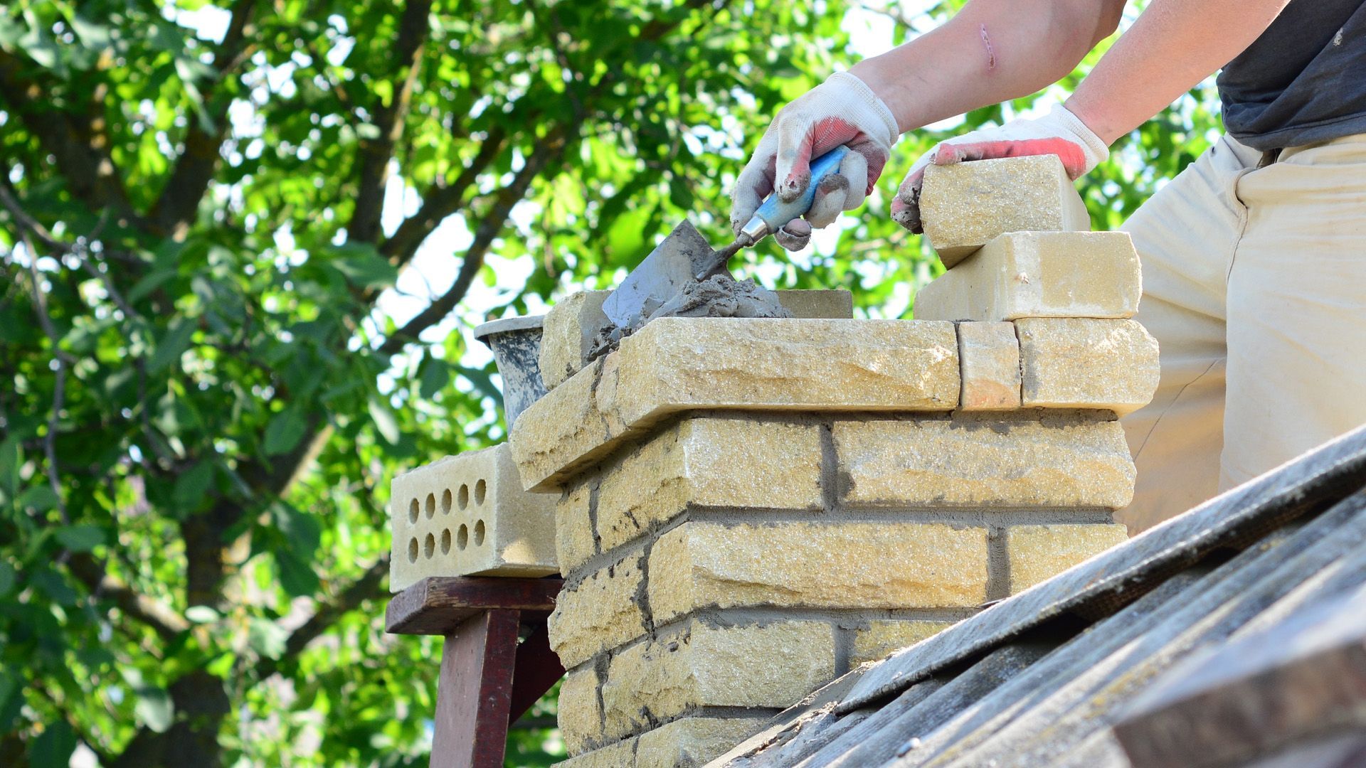 A man is laying bricks on top of a chimney.