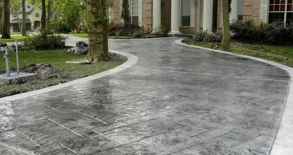 A concrete driveway leading to a house with trees in the background.