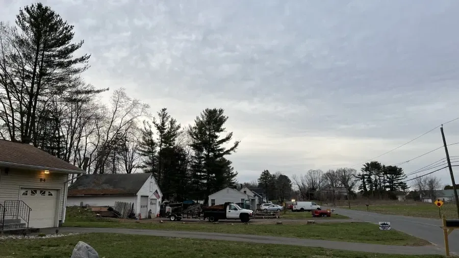 A cloudy day over a rural residential street with houses, trees, a white truck, and a grassy lot.
