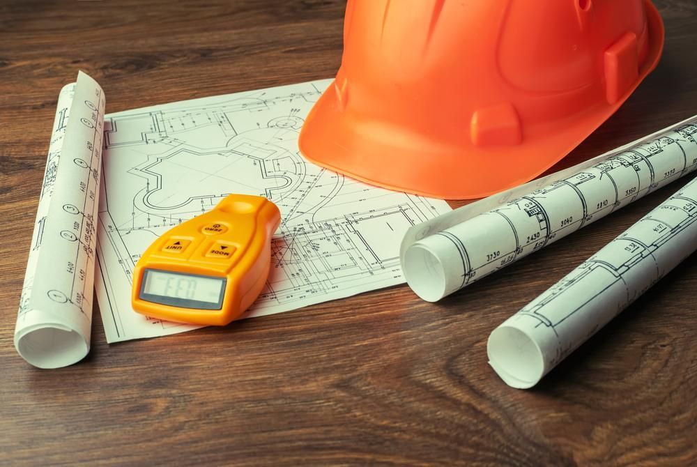 A Hard Hat , a Calculator , and Rolls of Blueprints Are on a Wooden Table — TPF Industries in Blacks Beach, QLD