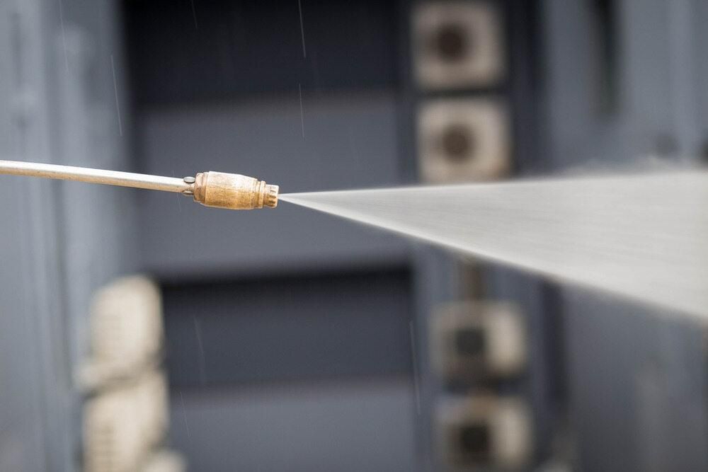 A Person is Using a High Pressure Washer to Clean a Building — TPF Industries in Blacks Beach, QLD