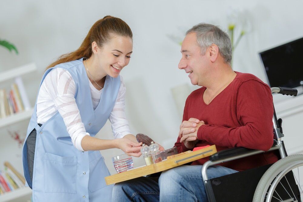 A Woman is Serving Food to a Man in a Wheelchair — TPF Industries in Sarina, QLD