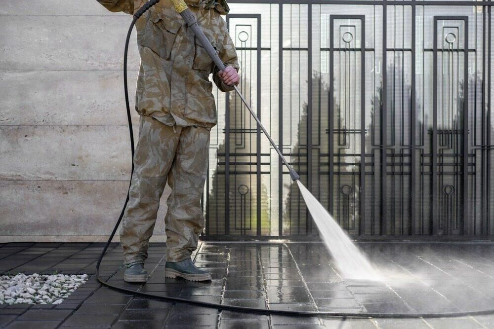 A Man is Using a High Pressure Washer to Clean a Fence — TPF Industries in Armstrong Beach, QLD