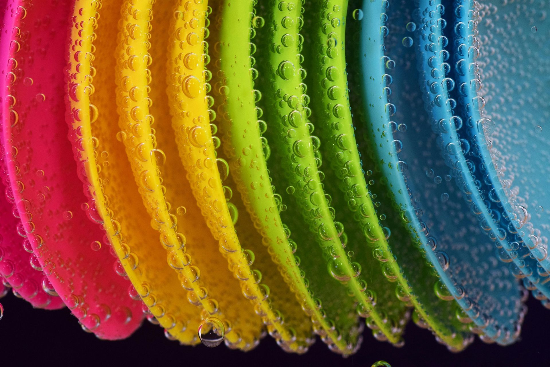 Rainbow-colored, curved plastic discs submerged in water, covered in bubbles.