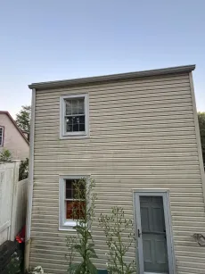 Two-story building with siding, two windows, and a door. Tan color with blue sky in the background.