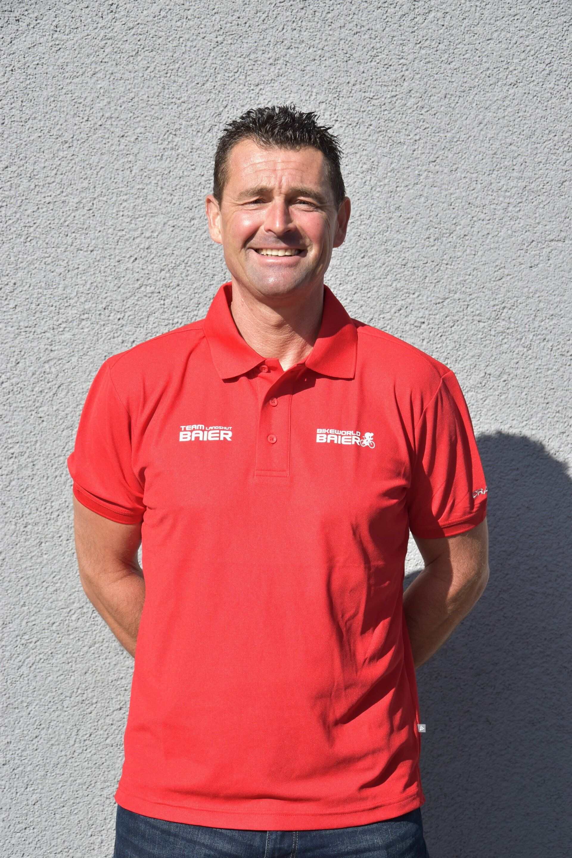 Ein Mann in einem roten Poloshirt steht vor einer Wand.