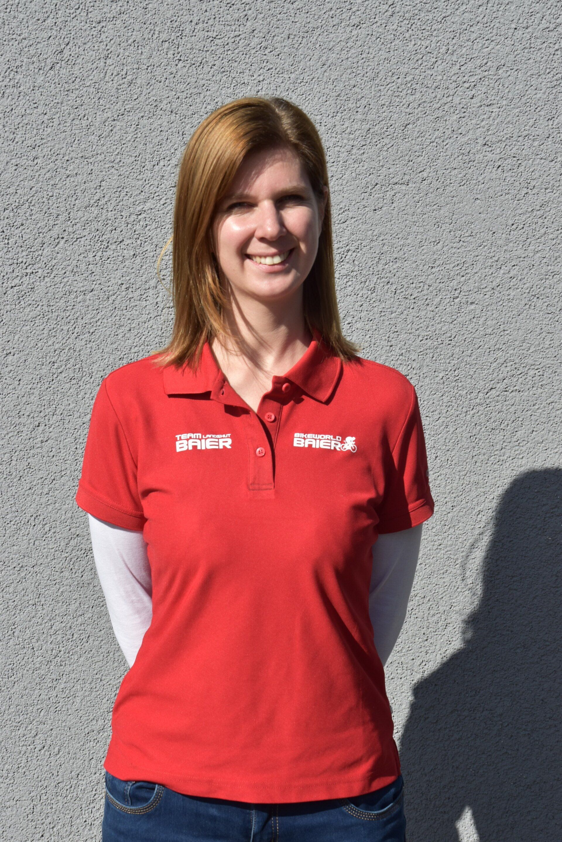 Eine Frau trägt ein rotes Poloshirt und lächelt.