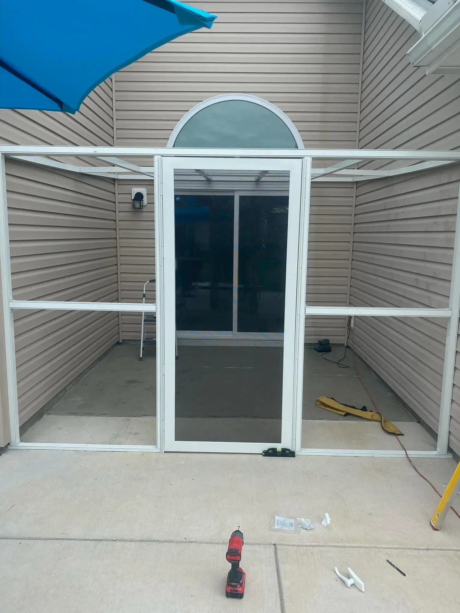 A screen door is being installed on a patio next to a house.