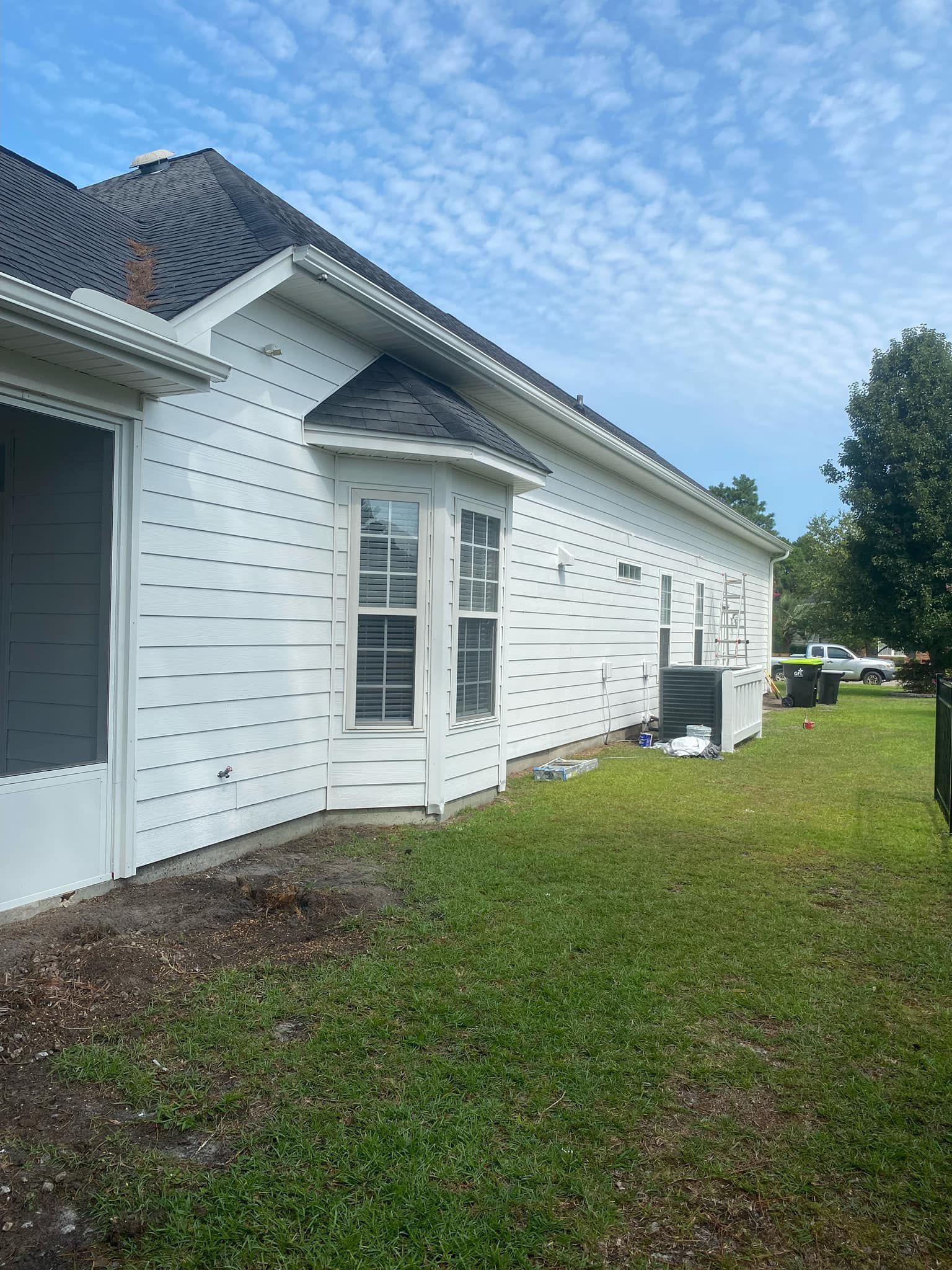 A white house with a black roof is sitting on top of a lush green field.