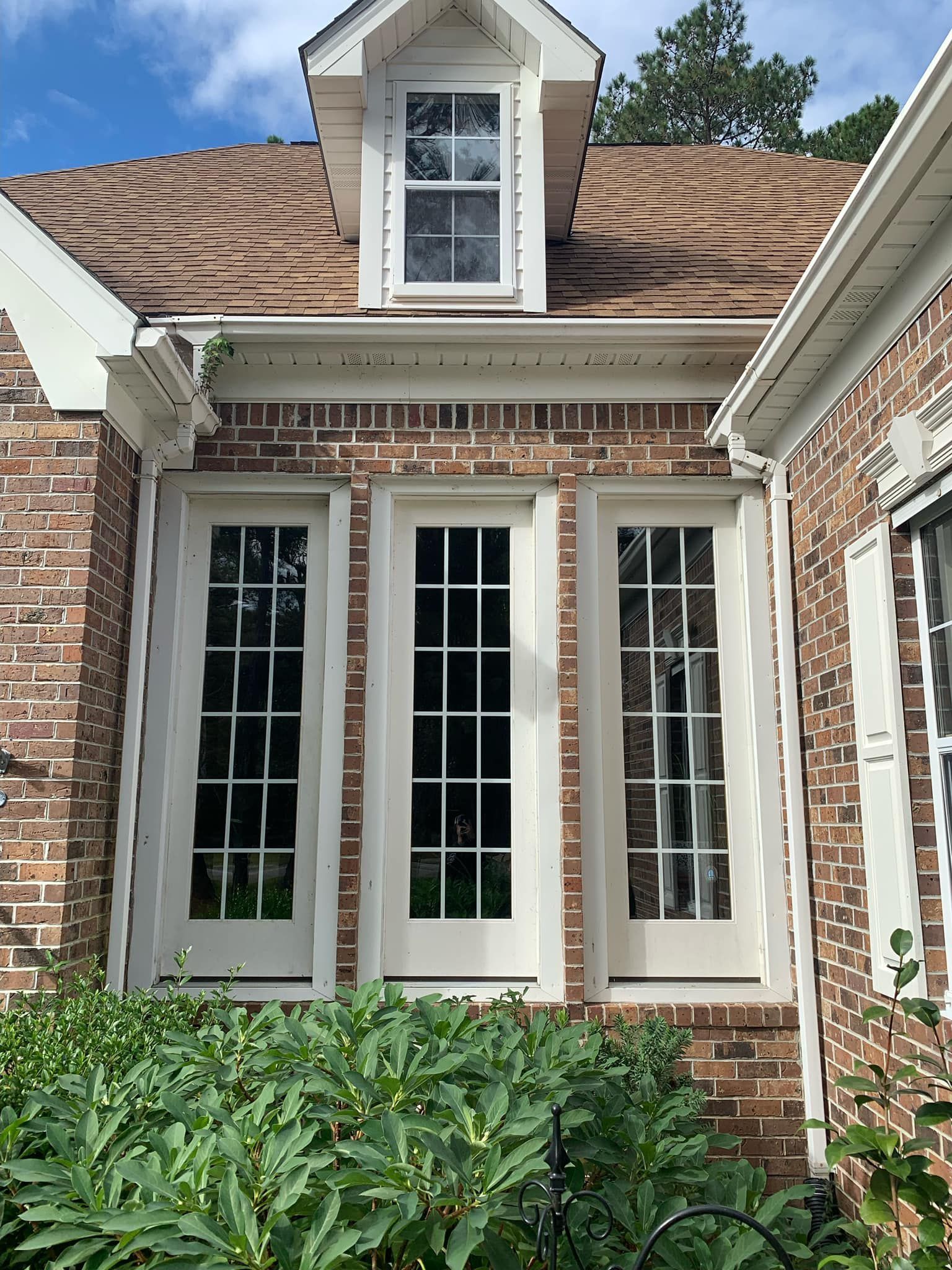 A brick house with white windows and shutters on a sunny day.
