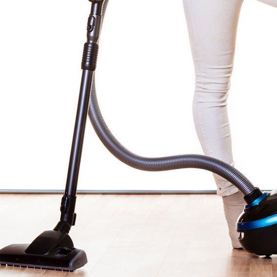 A woman is using a vacuum cleaner on a hardwood floor