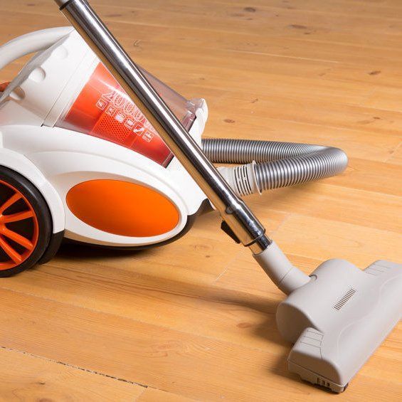 An orange and white vacuum cleaner is sitting on a wooden floor