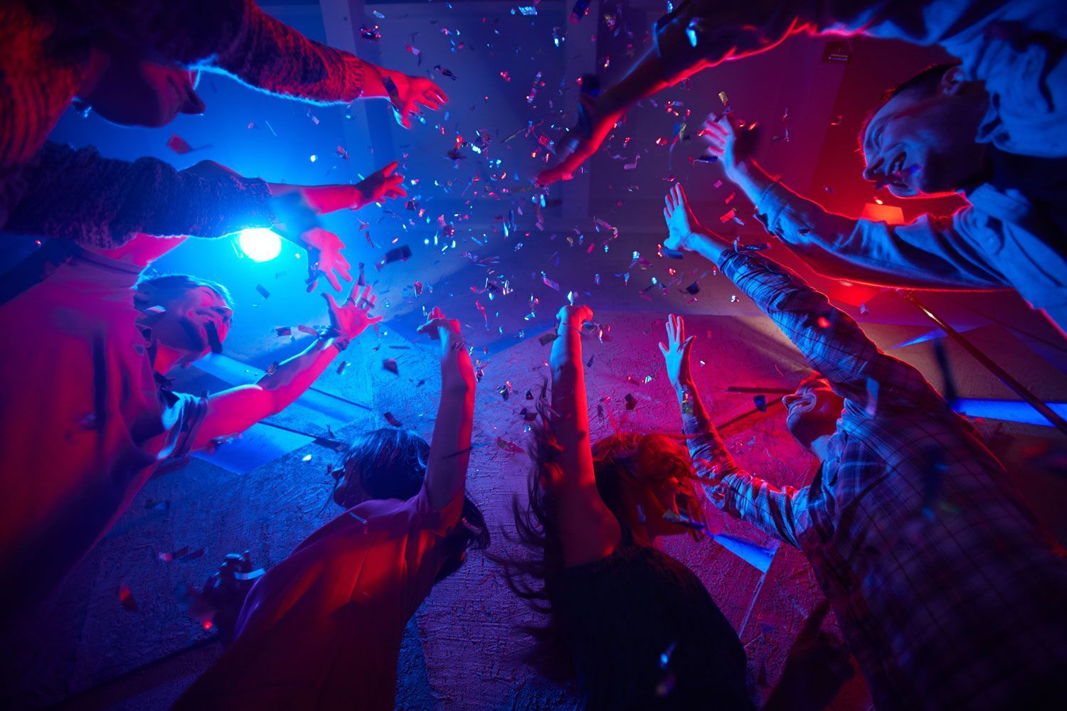 A group of people are dancing in a club with confetti falling from the ceiling.