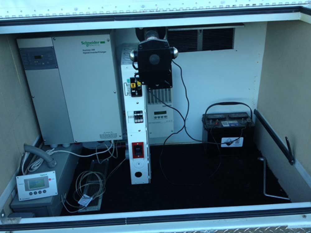 Interior of a utility box with electrical equipment: inverter, controller, battery, and monitoring screen.