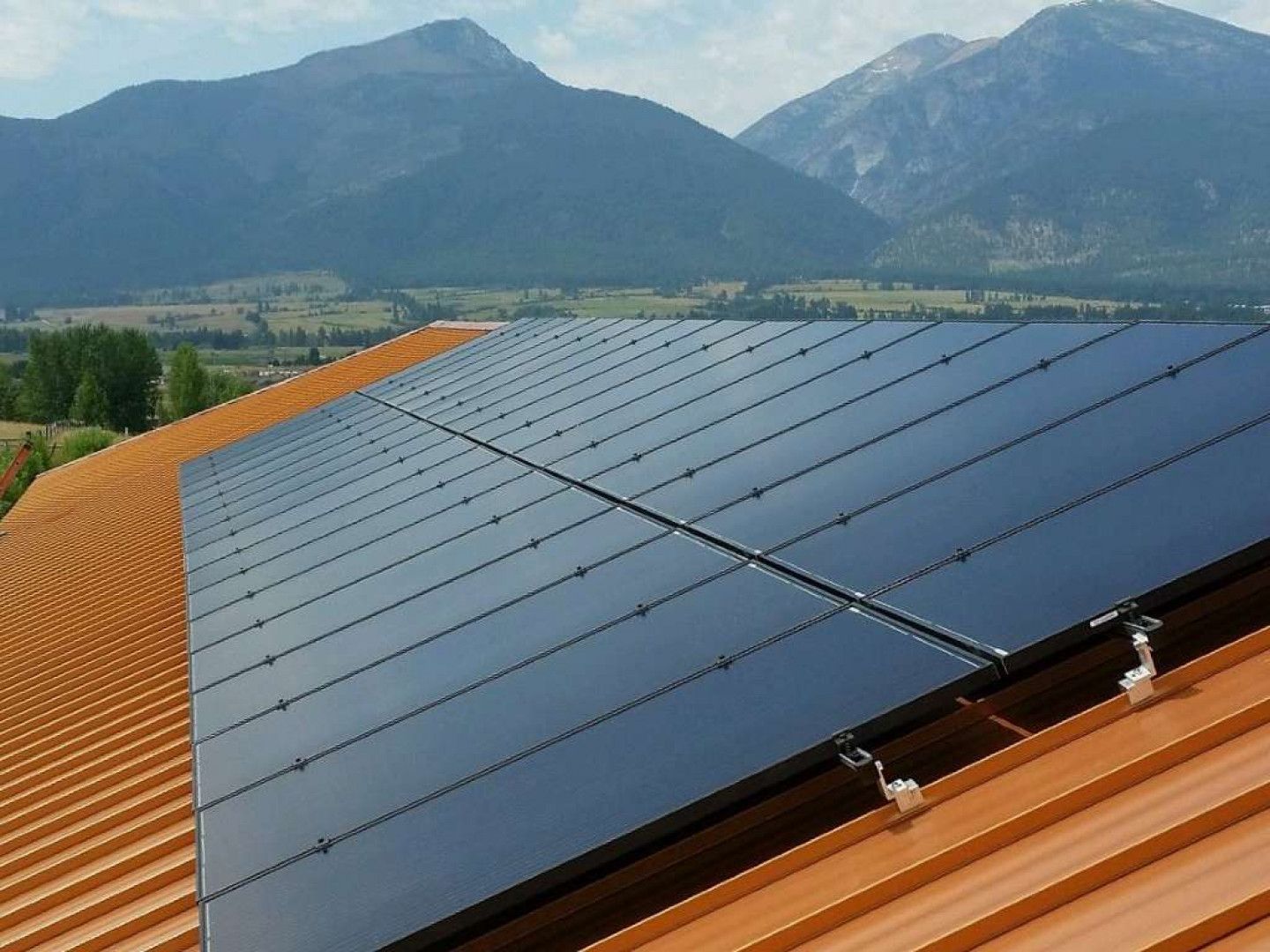 Solar panels on a rust-colored roof, mountains in the background.