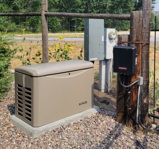 Tan outdoor generator next to electrical box on a post, set in a gravel area.